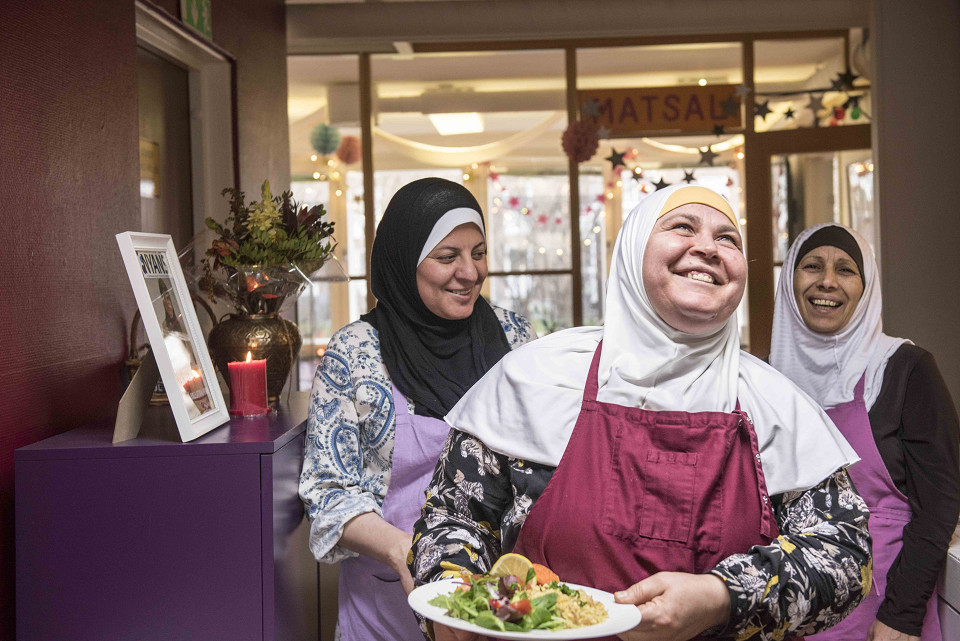 Tre glada kvinnor från utländsk bakgrund som bär sjal och håller en tallrik med Yalla Trappans catering, i samband med Första maj och social hållbarhet samt arbetet med arbetsintegration, inkludering och bättre arbetsvillkor för kvinnor långt från arbetsmarknaden i Malmö.