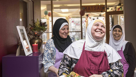 Tre glada kvinnor från utländsk bakgrund som bär sjal och håller en tallrik med Yalla Trappans catering, i samband med Första maj och social hållbarhet samt arbetet med arbetsintegration, inkludering och bättre arbetsvillkor för kvinnor långt från arbetsmarknaden i Malmö.